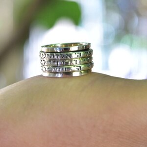 Puede incluir: Un conjunto de cinco anillos de plata apilados con letras hebreas grabadas en cada banda. Los anillos están apilados en el dedo de una persona.