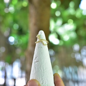 May include: A gold-toned ring with a twisted design, displayed on a white cone-shaped ring holder.