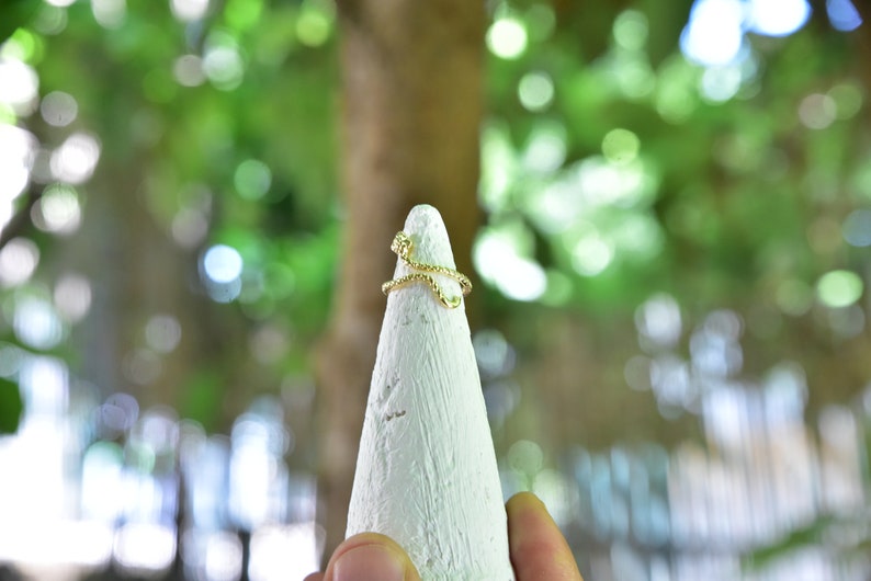 May include: A gold-toned ring with a twisted design, displayed on a white cone-shaped ring holder.