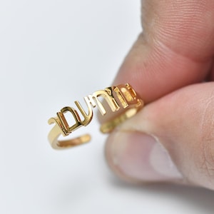 Puede incluir: Un anillo de oro con la palabra hebrea "שלום" (shalom) escrita en letras en relieve.