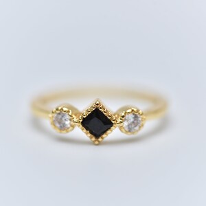 May include: A gold ring with three stones. The center stone is a black square, and the two stones on either side are round and white.