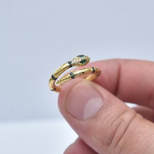 May include: A gold snake ring with green and black stones. The ring is designed to wrap around the finger.