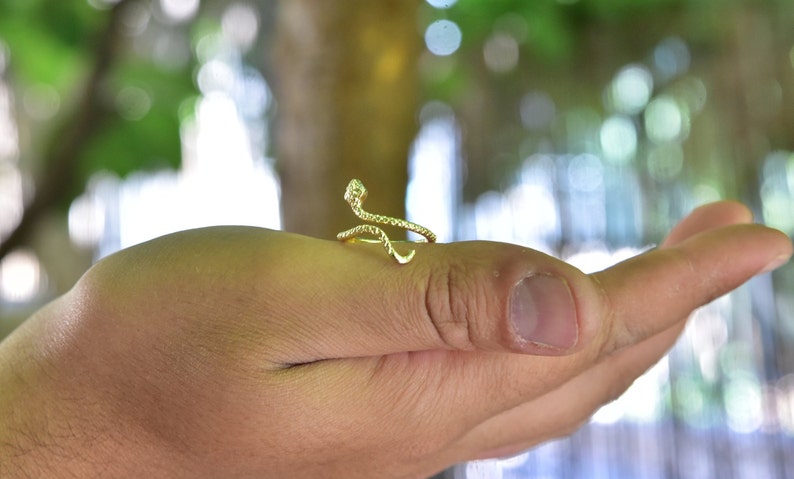 May include: A gold snake ring with a coiled design. The ring is on a person's hand.