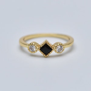 May include: A gold ring with three stones. The center stone is a black square, and the two stones on either side are round and white.