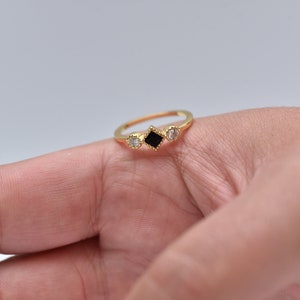 May include: A gold ring with three stones. The center stone is a black square, and the two stones on either side are round and clear.