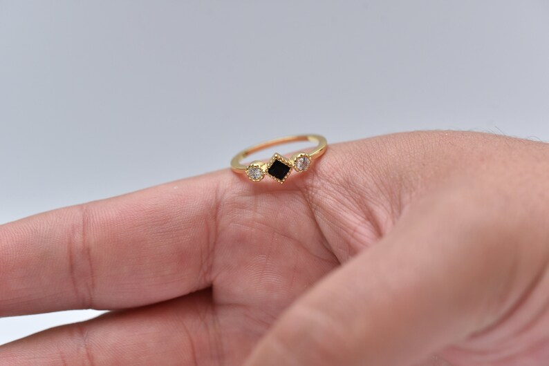 May include: A gold ring with three stones. The center stone is a black square, and the two stones on either side are round and clear.