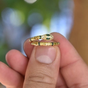 May include: A gold snake ring with green and white stones. The snake is coiled and the head is facing forward.