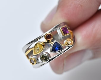 May include: A silver and gold ring with a variety of colorful gemstones, including blue, yellow, pink, and green.