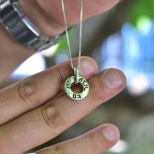 May include: A silver chain necklace with a round pendant inscribed with Hebrew text. The pendant is held by a person's hand, and a silver ring with a lion design is on a finger on the same hand.