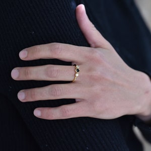 May include: A gold ring with three small stones. The center stone is black and square, and the two stones on either side are round and white.
