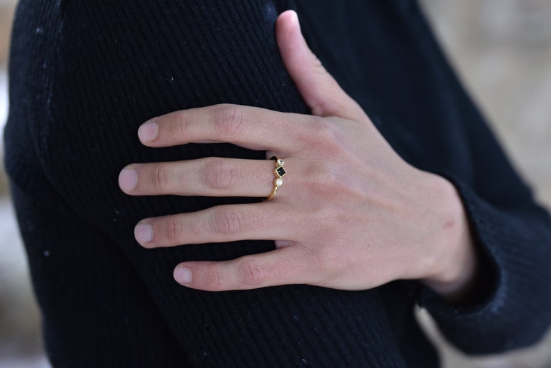 May include: A gold ring with three small stones. The center stone is black and square, and the two stones on either side are round and white.
