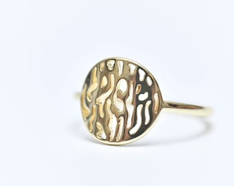May include: A gold ring with a large, round, openwork design. The design is a repeating pattern of swirls and lines.