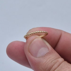 Könnte beinhalten: Ein dünner goldener Ring mit einem Perlenmuster.