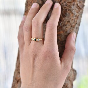 May include: A gold ring with a black square-shaped stone and two smaller round white stones.