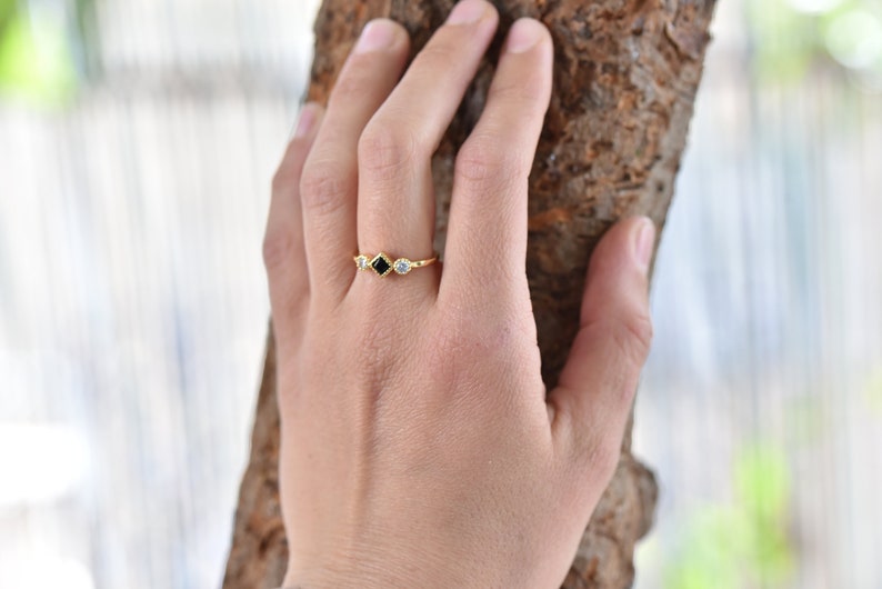 May include: A gold ring with a black square-shaped stone and two smaller round white stones.