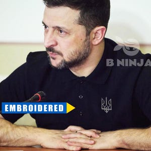 Puede incluir: Un hombre con una camisa polo negra con un símbolo de tridente ucraniano bordado. El texto "EMBROIDERED" es visible en la imagen.