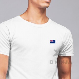 May include: A white t-shirt with a small New Zealand flag printed on the right side of the chest.