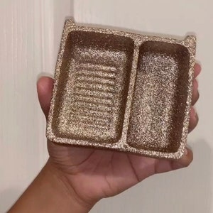 Op de afbeelding: Een rechthoekig dienblad bedekt met roségouden glitters, voorzien van twee aparte vakken. Het grotere linkervak heeft een reeks horizontale ribbels op de bodem, terwijl het smallere rechtervak een gladde, vlakke bodem heeft.