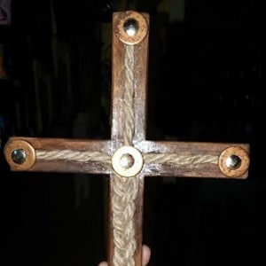 May include: A wooden cross with a rope design and brass accents. The cross is brown and the rope is a natural beige color.