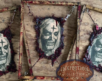 Könnte beinhalten: Drei gerahmte Horror-Wanddekorationen mit einer blutigen, zerrissenen und abgenutzten Ästhetik. Jeder Rahmen zeigt ein Schwarzweißbild einer blassen Figur mit einem Kreuz auf der Stirn. Die Rahmen sind mit roten Farbstichen abgenutzt und haben einen goldfarbenen Rahmen. Der untere Rahmen trägt ein Logo mit der Aufschrift "INKFECTION COLLECTION".