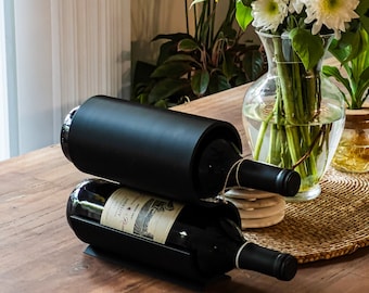 May include: A black metal wine rack holds two bottles of red wine on a wooden table. The bottles are labeled with a white label and have a black cap.