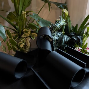 May include: A black, flexible, modular wine rack with three slots for bottles. The rack is made of a soft, pliable material and is designed to fit snugly around the bottles.