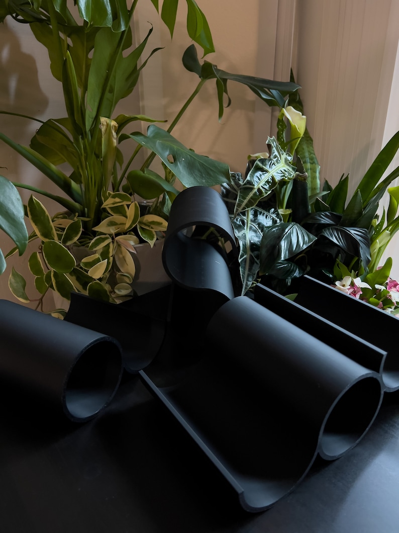 May include: A black, flexible, modular wine rack with three slots for bottles. The rack is made of a soft, pliable material and is designed to fit snugly around the bottles.