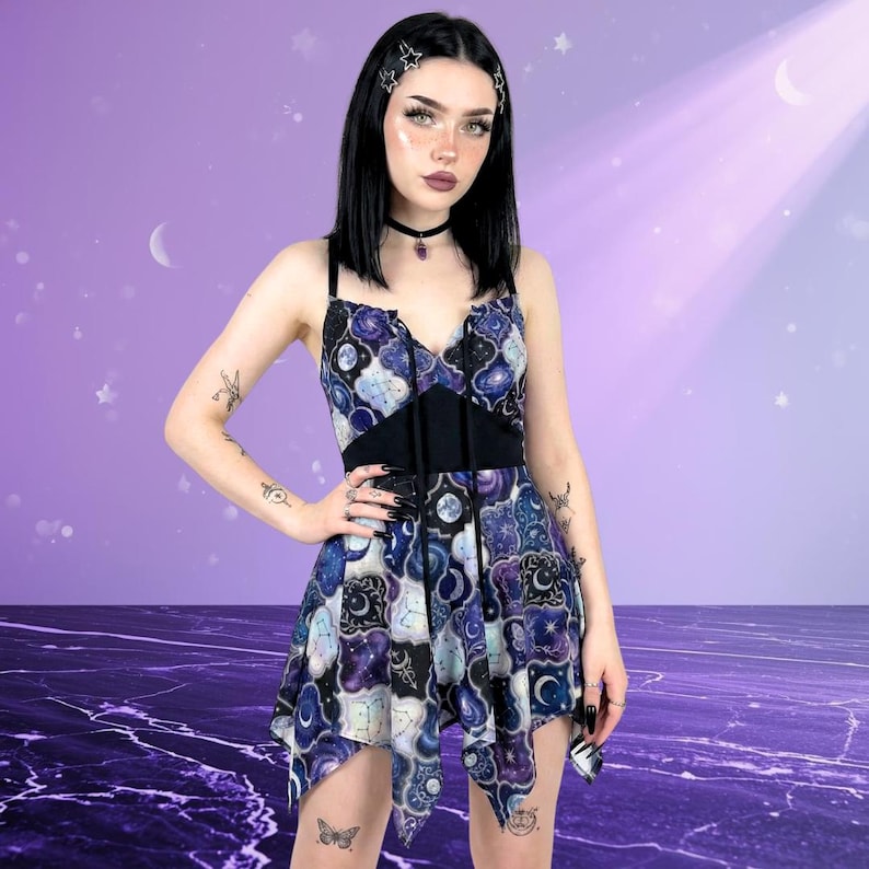 May include: A sleeveless dress with a celestial pattern in shades of blue, purple, and white. The dress features a black bodice and a flowing, asymmetrical hemline. The dress is adorned with a moon and star design.