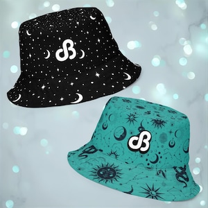 May include: Two bucket hats. One is black with a white celestial pattern of stars and moons. The other is teal with a celestial pattern of suns, moons, and stars. Both hats have a white logo.