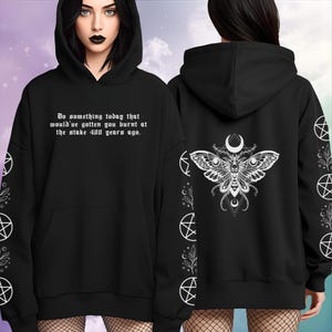 Peut inclure: Sweat &agrave; capuche noir avec poche avant. Le devant affiche le texte : "Faites quelque chose aujourd'hui qui vous aurait fait br&ucirc;ler sur le b&ucirc;cher il y a 400 ans." Le dos pr&eacute;sente un motif de papillon blanc avec une lune. Manches avec pentagrammes blancs.