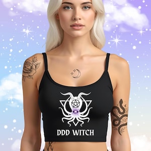 May include: Black crop top with spaghetti straps featuring a white graphic design of a pentagram, horns, and tentacles, with the text "DDD WITCH" in white. The top is worn by a person with tattoos.