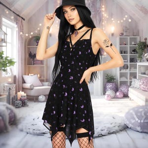 May include: Black dress patterned with purple crescent moons. The dress features a V-neck and spaghetti straps. The hem is asymmetrical. The model is wearing a black hat and choker.