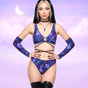 May include: A galaxy-print two-piece set, comprising a V-neck top with a keyhole and high-waisted bottoms, plus matching arm sleeves. The fabric is blue, purple, and white, with a celestial design. The outfit is designed for a striking look.