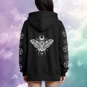 Peut inclure: Sweat &agrave; capuche noir avec un motif de papillon blanc d&eacute;taill&eacute; dans le dos, orn&eacute; d'un croissant de lune et de motifs g&eacute;om&eacute;triques. Les manches pr&eacute;sentent des pentagrammes blancs et des motifs botaniques. Le sweat &agrave; capuche est de couleur fonc&eacute;e.