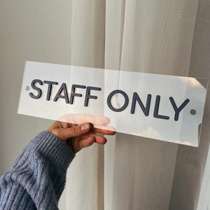 May include: A clear acrylic sign with black lettering that reads "STAFF ONLY".