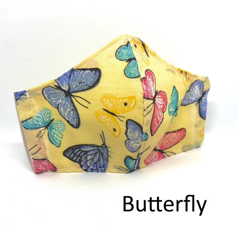 May include: A yellow fabric face mask with a colorful butterfly print. The mask has a three-dimensional shape and is made of cotton.
