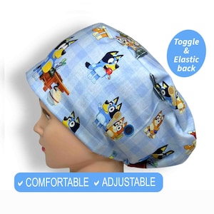 K&ouml;nnte beinhalten: Eine hellblaue OP-Haube mit Vichy-Muster und Zeichentrickfiguren. Die Haube tr&auml;gt den Text "Toggle & Elastic back" und "COMFORTABLE ADJUSTABLE".