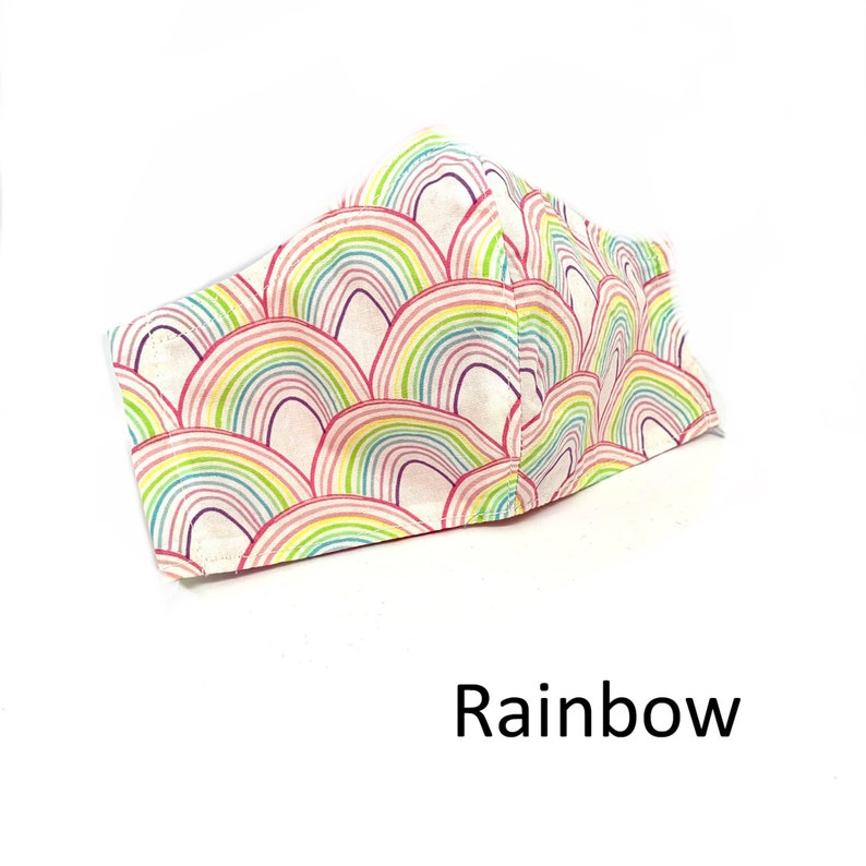 May include: A white face mask with a rainbow pattern. The pattern is made up of multiple rainbow arches that are stacked on top of each other. The mask is made of fabric and has a white background. The text "Rainbow" is written below the mask.