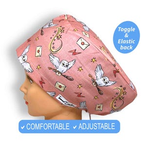 May include: Pink surgical scrub hat with a white owl and stars pattern. The hat has an adjustable toggle and elastic back. The text "COMFORTABLE" and "ADJUSTABLE" is printed on the bottom of the image.