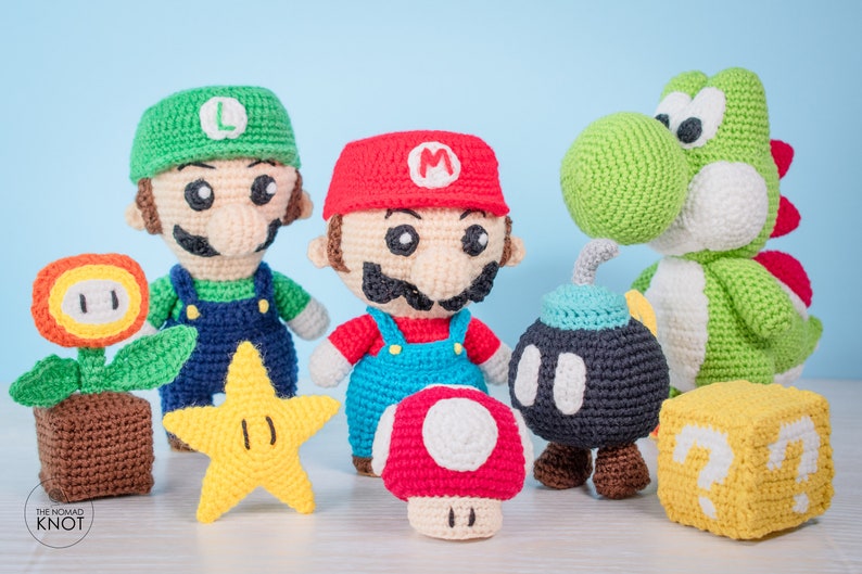 May include: Crocheted plush toys of characters from the Super Mario video game series. The characters include Mario, Luigi, Yoshi, a bomb, a star, a mushroom, and a question block.