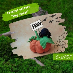 May include: Crochet pattern for a "Tiny spider" amigurumi toy. The spider is sitting on a crocheted pumpkin with a "Boo!" sign. The pattern is available in English and PDF format.