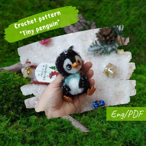Könnte beinhalten: Häkelanleitung für ein kleines Amigurumi-Pinguin-Spielzeug. Der Pinguin ist schwarz-weiß mit einem blauen Schal und hält ein kleines Geschenk. Die Anleitung ist in englischer Sprache und im PDF-Format verfügbar.