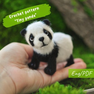 May include: Crochet pattern for a tiny panda amigurumi. The pattern is written in English and is available as a PDF download. The image shows a crocheted panda in a hand, with black and white fur.