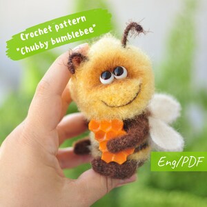 Könnte beinhalten: Häkelanleitung für ein Amigurumi-Spielzeug "Chubby Bumblebee". Die Biene ist gelb und braun mit weißen Flügeln und hält eine Honigwabe. Die Anleitung ist in englischer Sprache und im PDF-Format verfügbar.