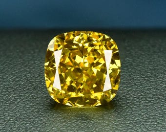 May include: A square-cushion cut yellow diamond, displayed on a dark, textured surface with a blue backdrop. The gemstone's facets catch the light, producing a bright display of colour and sparkle. The image evokes luxury and fine jewellery.