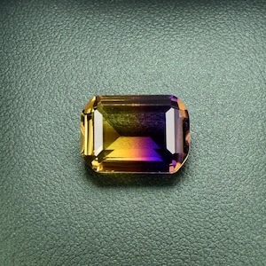 May include: A green leather ring box with a yellow, orange, and purple gemstone inside.