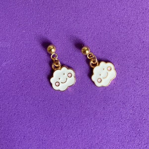 May include: A pair of gold earrings with a white cloud charm featuring a pink smiling face.