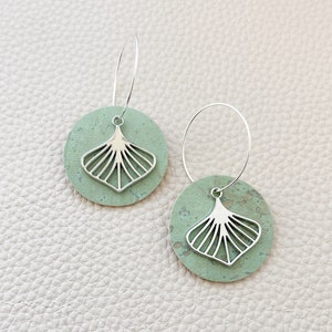 May include: A pair of silver hoop earrings with a green cork circle pendant featuring a silver cutout of a fan shape.