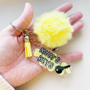 May include: A yellow fluffy pom-pom keyring with a clear acrylic tag that says "Mum's Keys" in black lettering with a black keyhole graphic.