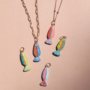 May include: Two gold-tone metal necklaces with fish-shaped pendants and three additional loose fish charms. The fish are painted in vibrant colors including red, yellow, blue, and green with polka dot patterns and small metal jump rings for attachment.